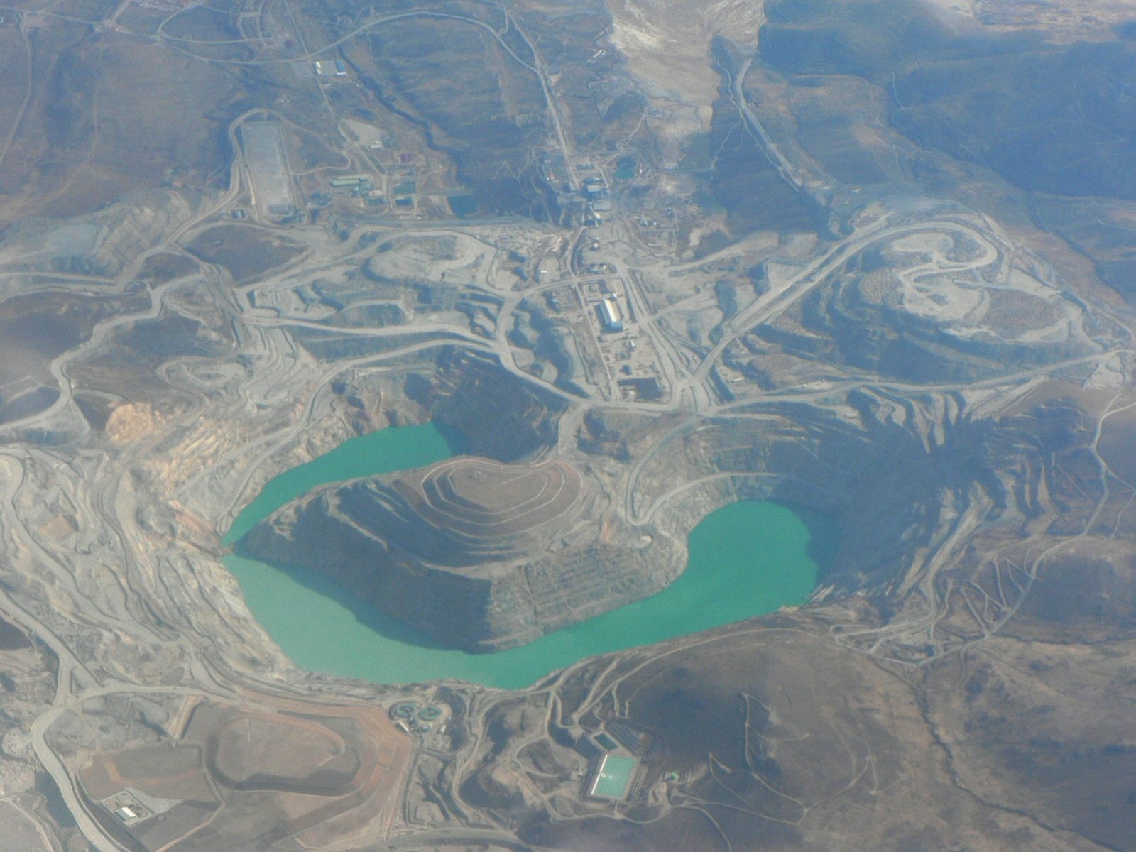 Aerial view of the Tintaya open-pit copper mine in Peru, showing benched pit walls and a turquoise pit lake surrounded by waste rock and haul roads.